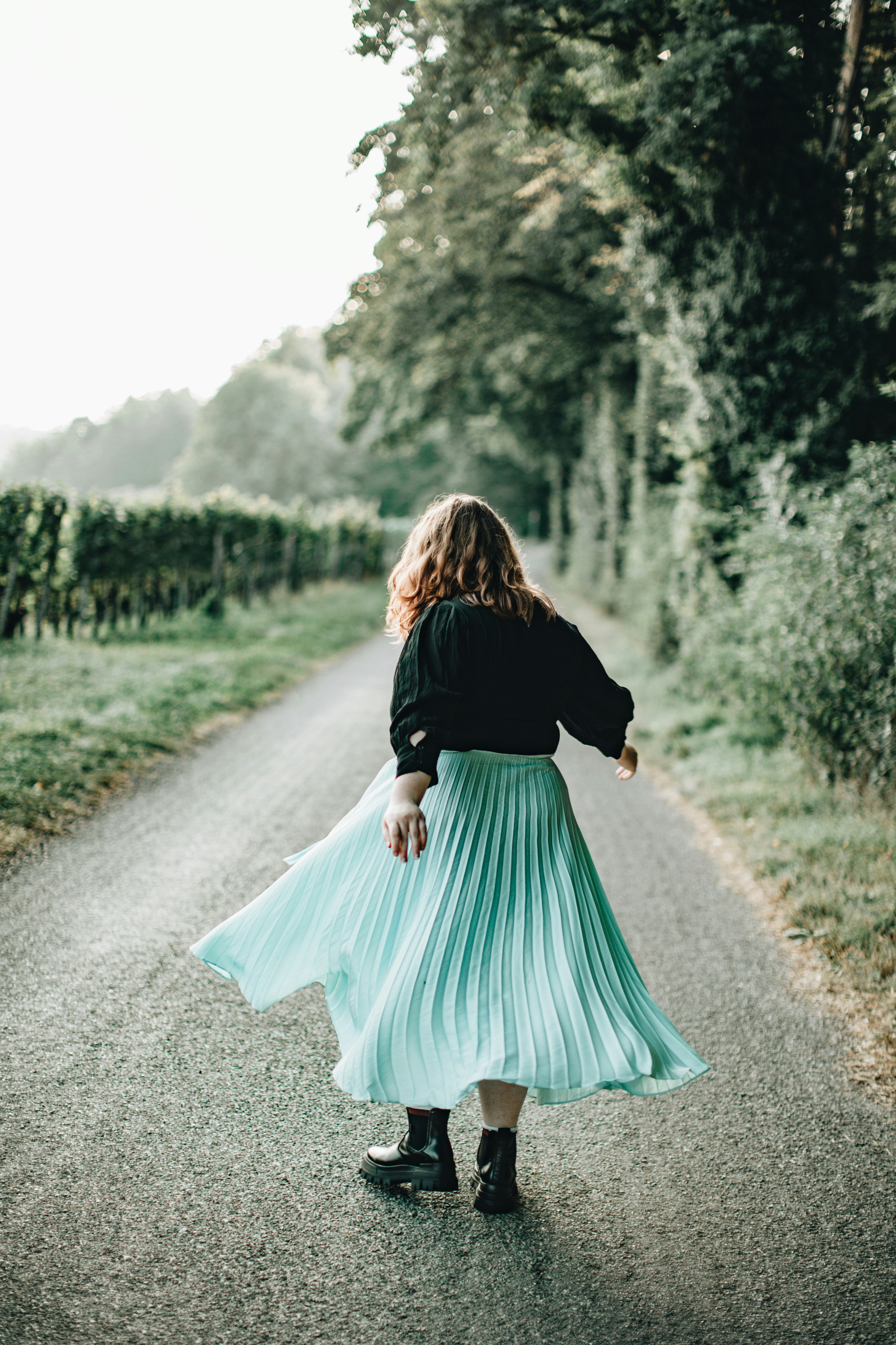 woman in black long sleeve shirt and teal skirt walking on dirt road during daytime