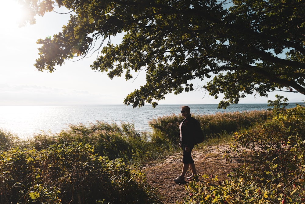 man in black jacket walking on green grass field near body of water during daytime