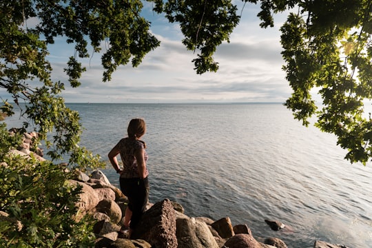 woman in black tank top and black pants standing on brown rock near body of water in Jastarnia Poland