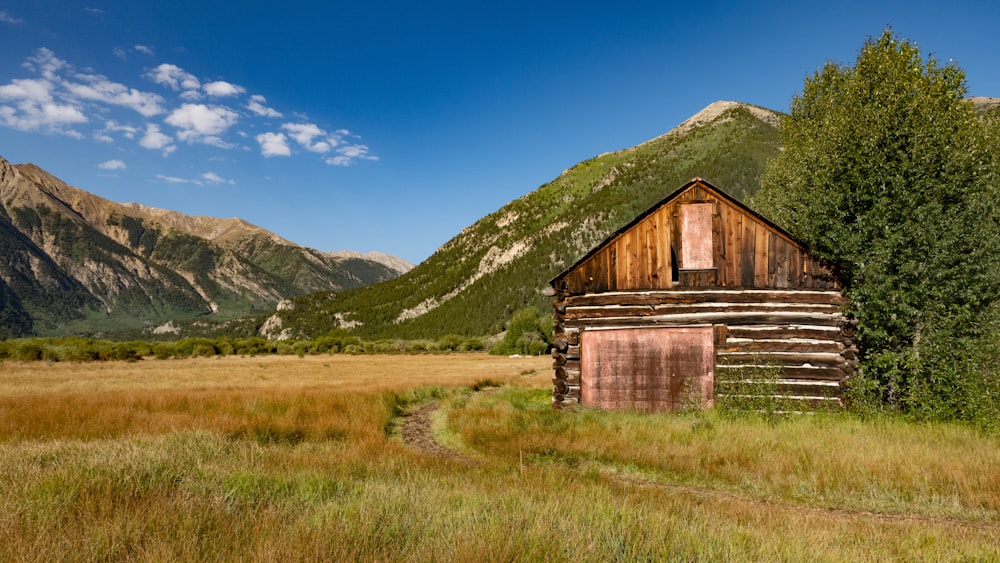brown wooden house on green grass field near mountain under blue sky during daytime