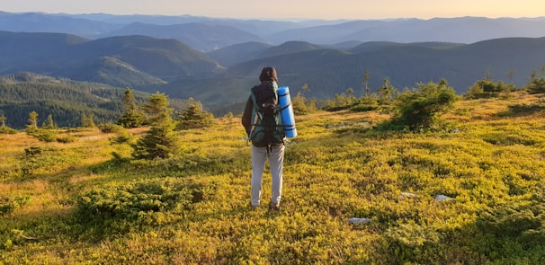 A backpacker setting up camp on a rocky peak overlooking a vast mountain range under a clear sky.