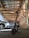 An electric scooter is parked inside a spacious garage with a slanted wooden roof and exposed brick walls. Several cars are also parked inside, and the lighting is provided by natural light coming through the openings.