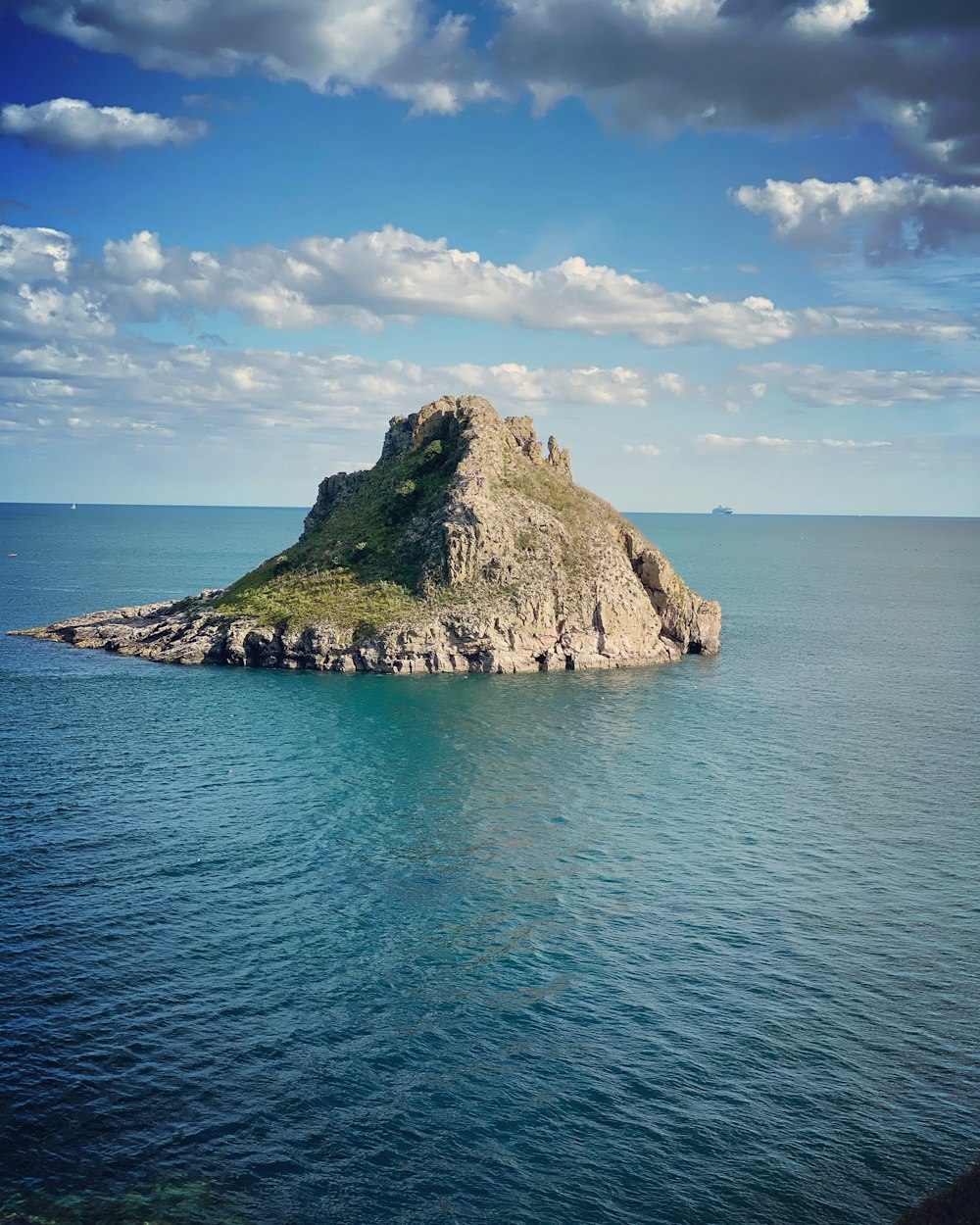 green and brown rock formation on blue sea under blue and white cloudy sky during daytime