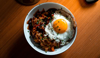 A close-up shot of a steaming bowl of colorful fried rice topped with fresh herbs and a perfectly cooked egg.