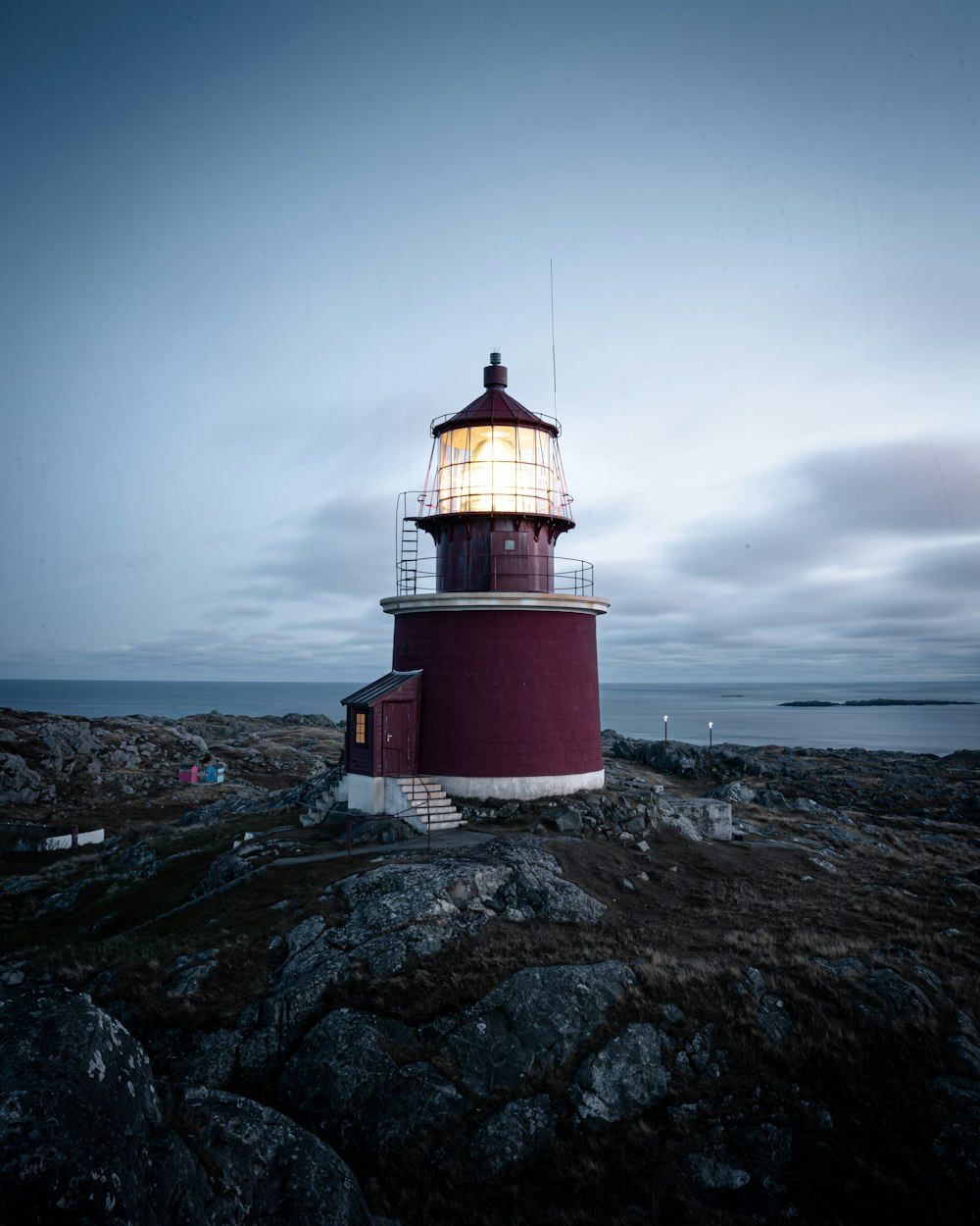 red and white lighthouse on gray rocky mountain under gray cloudy sky