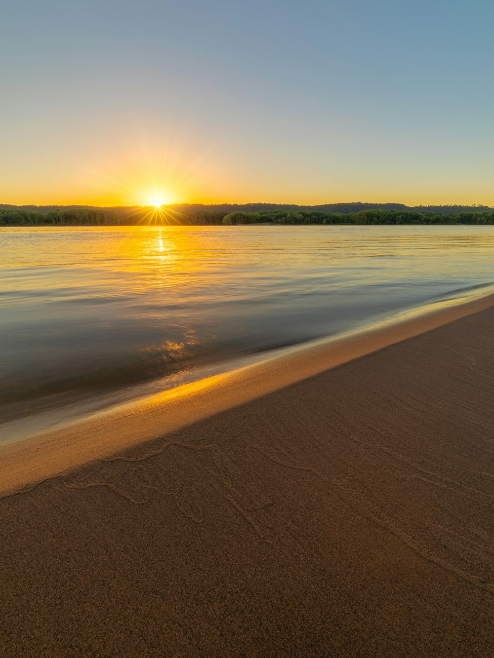 body of water near green trees during sunset