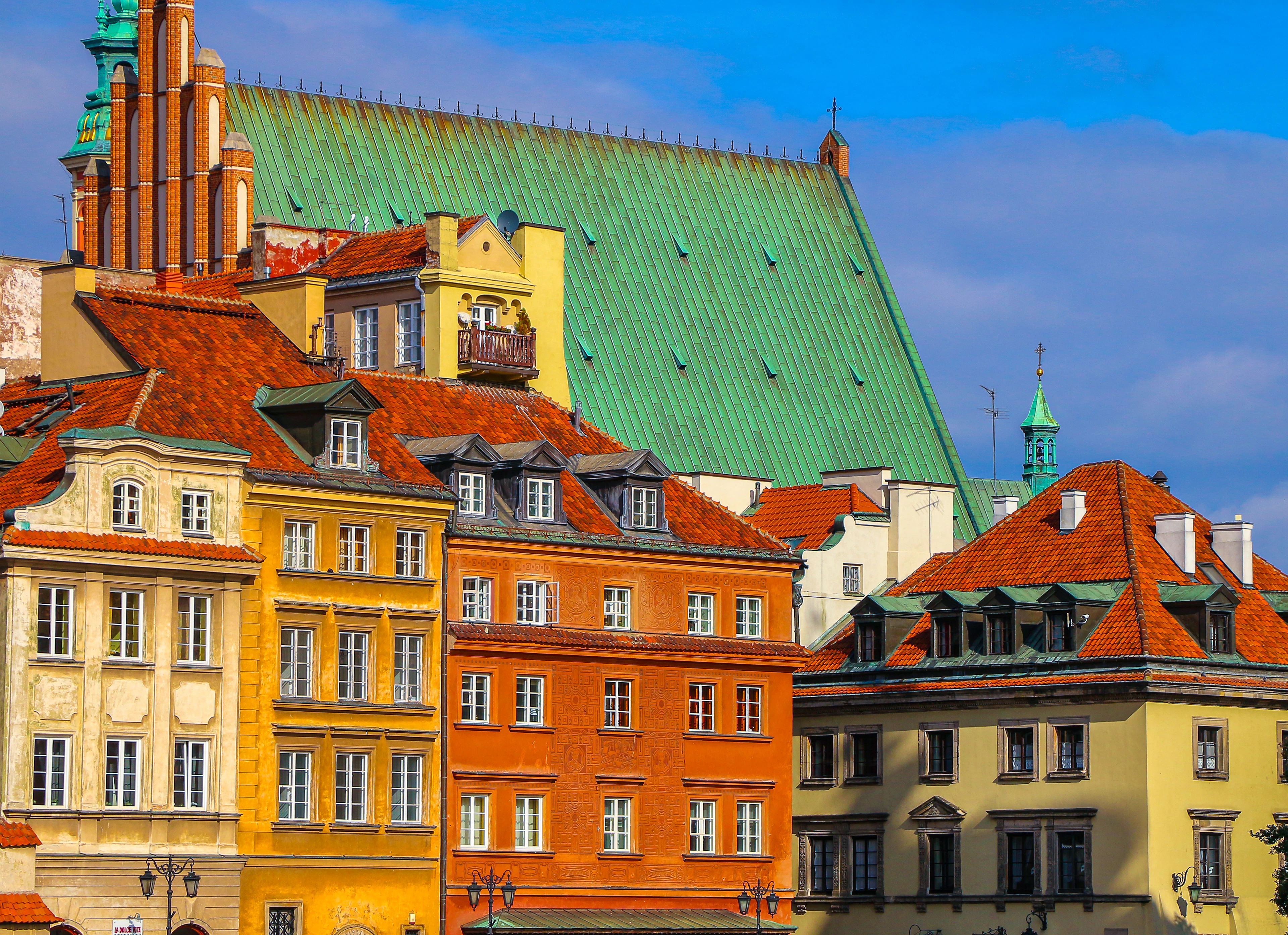 Colorful row houses with steep tiled roofs and a green-domed cathedral in Warsaw's Old Town skyline