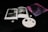 An open book with black and white images of interior designs lies on a dark surface. Next to it, a small abstract painting features swirling tones of pink and purple. A few stones and two small objects resembling earrings are neatly arranged on a white speckled plate.