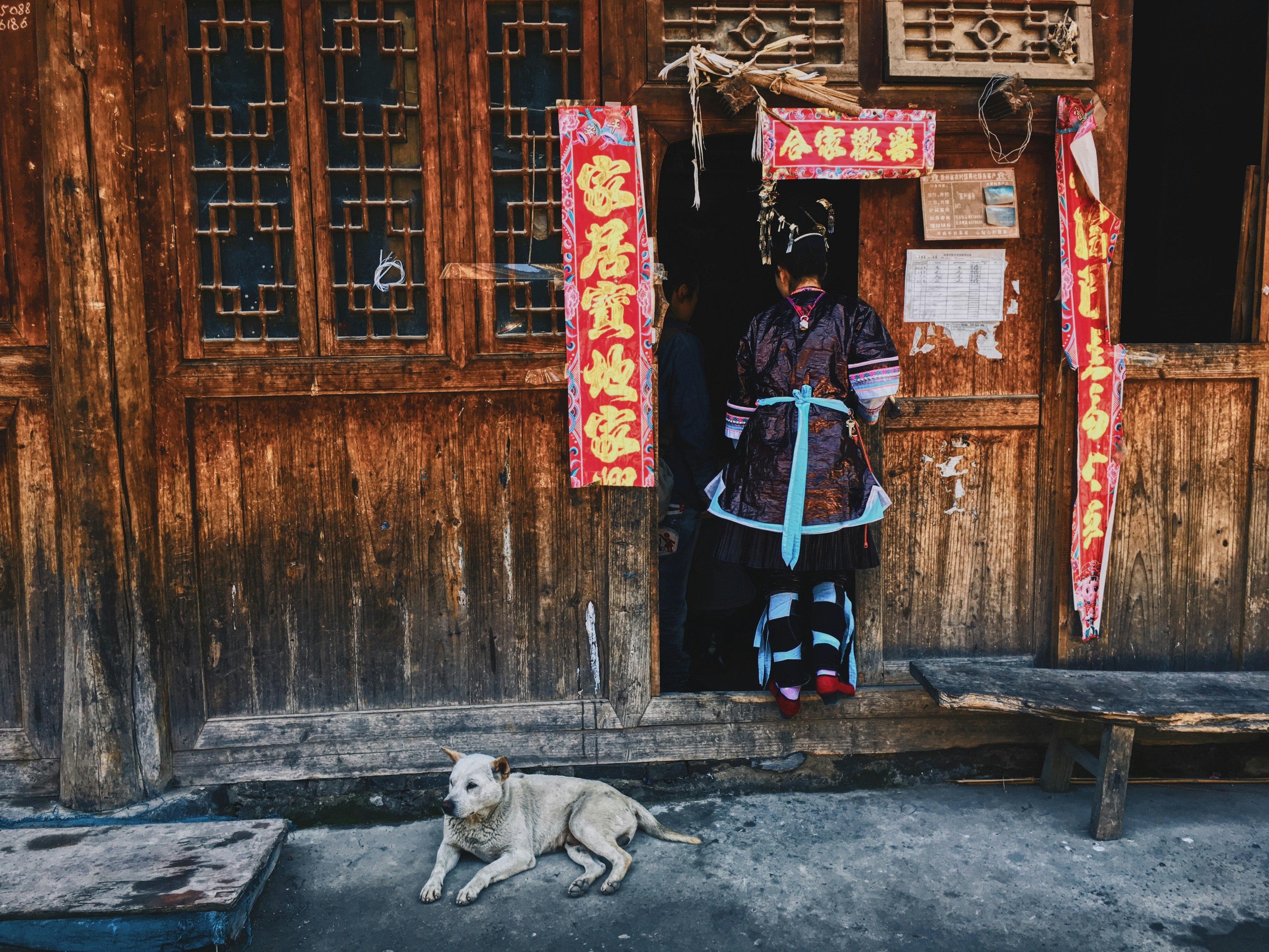 woman in black jacket and blue pants standing beside brown wooden door during daytime