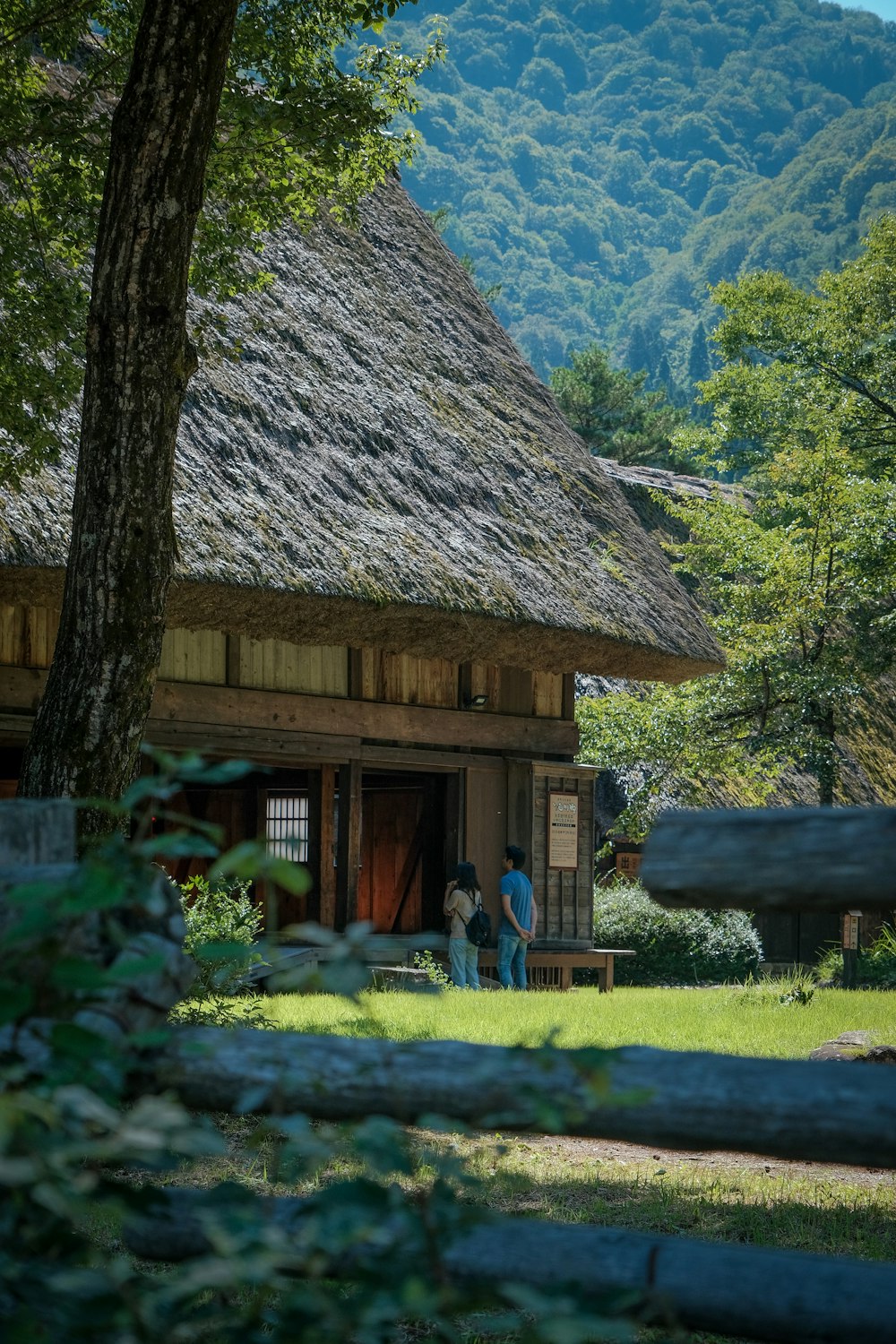 昼間、茶色の木造住宅の近くのベンチに座っている2人