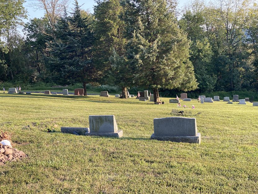 A serene, custom-designed headstone in a sunlit cemetery surrounded by flowers.