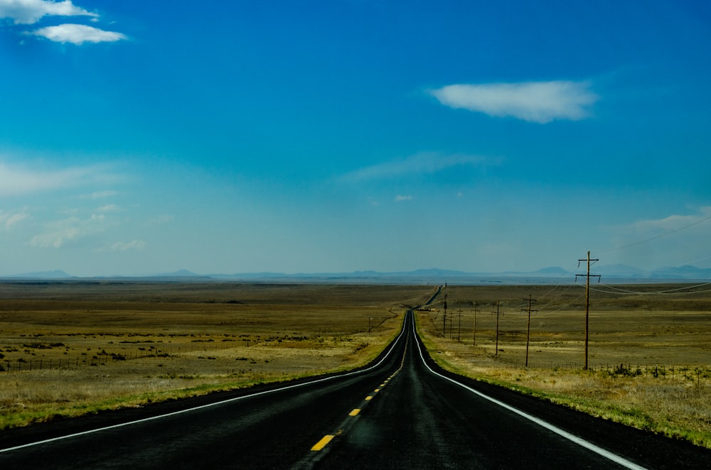 black asphalt road between brown grass field under blue sky during daytime