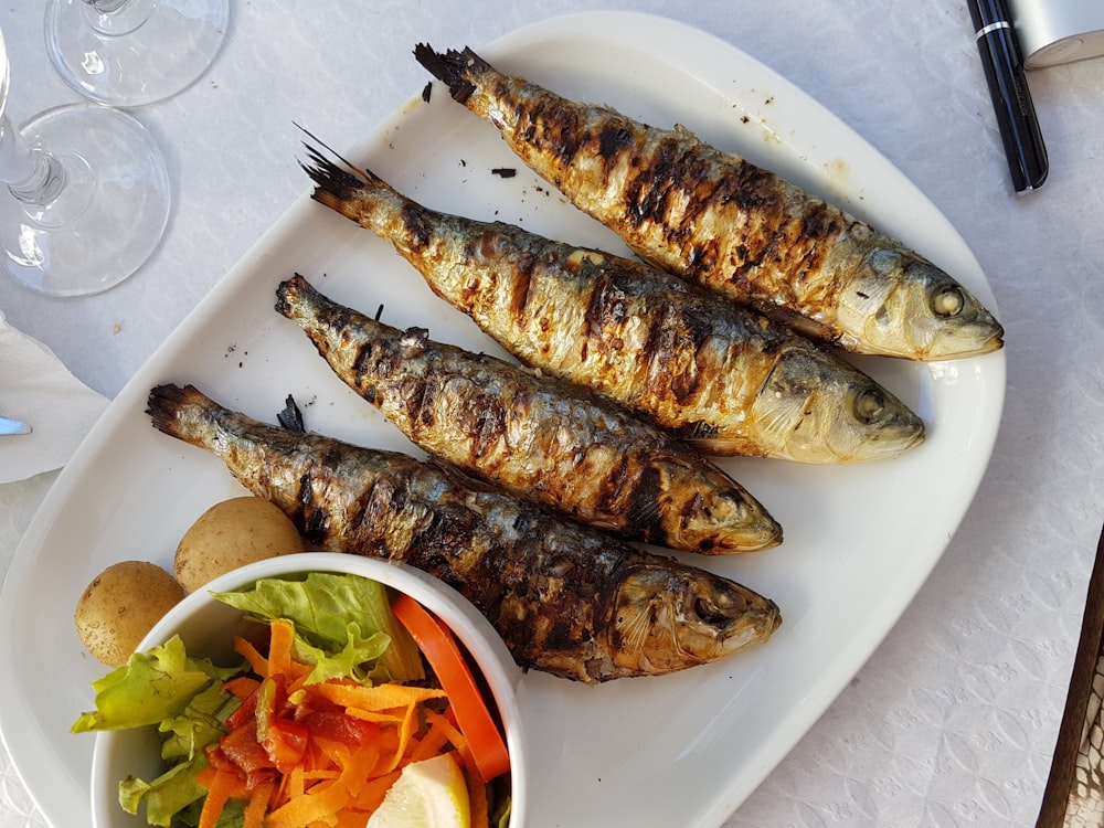 Pesce alla griglia con insalata di verdure su piatto in ceramica bianca