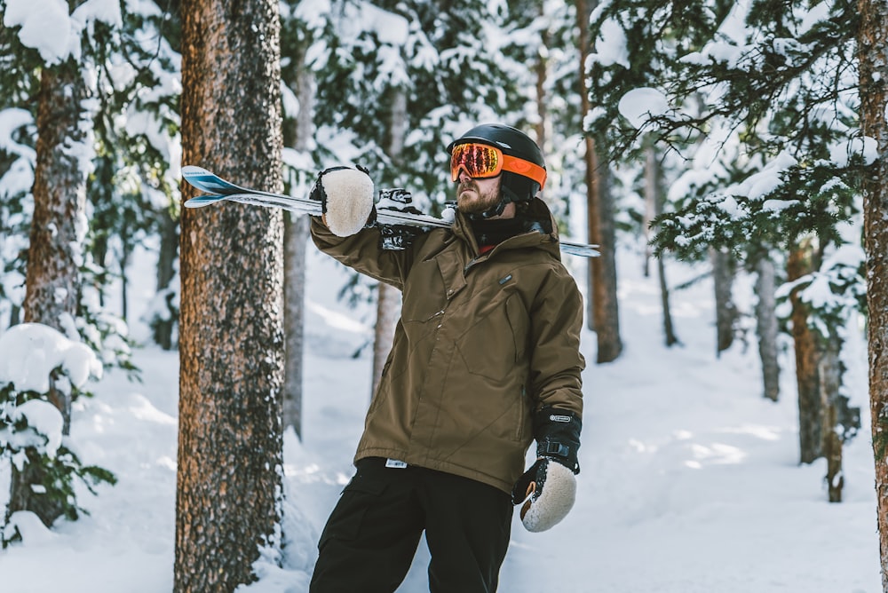 hombre con chaqueta marrón y pantalones negros sosteniendo un bastón de esquí de nieve blanco y negro