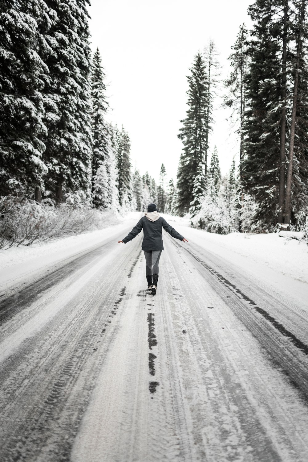 Persona con chaqueta negra caminando por la carretera cubierta de nieve durante el día