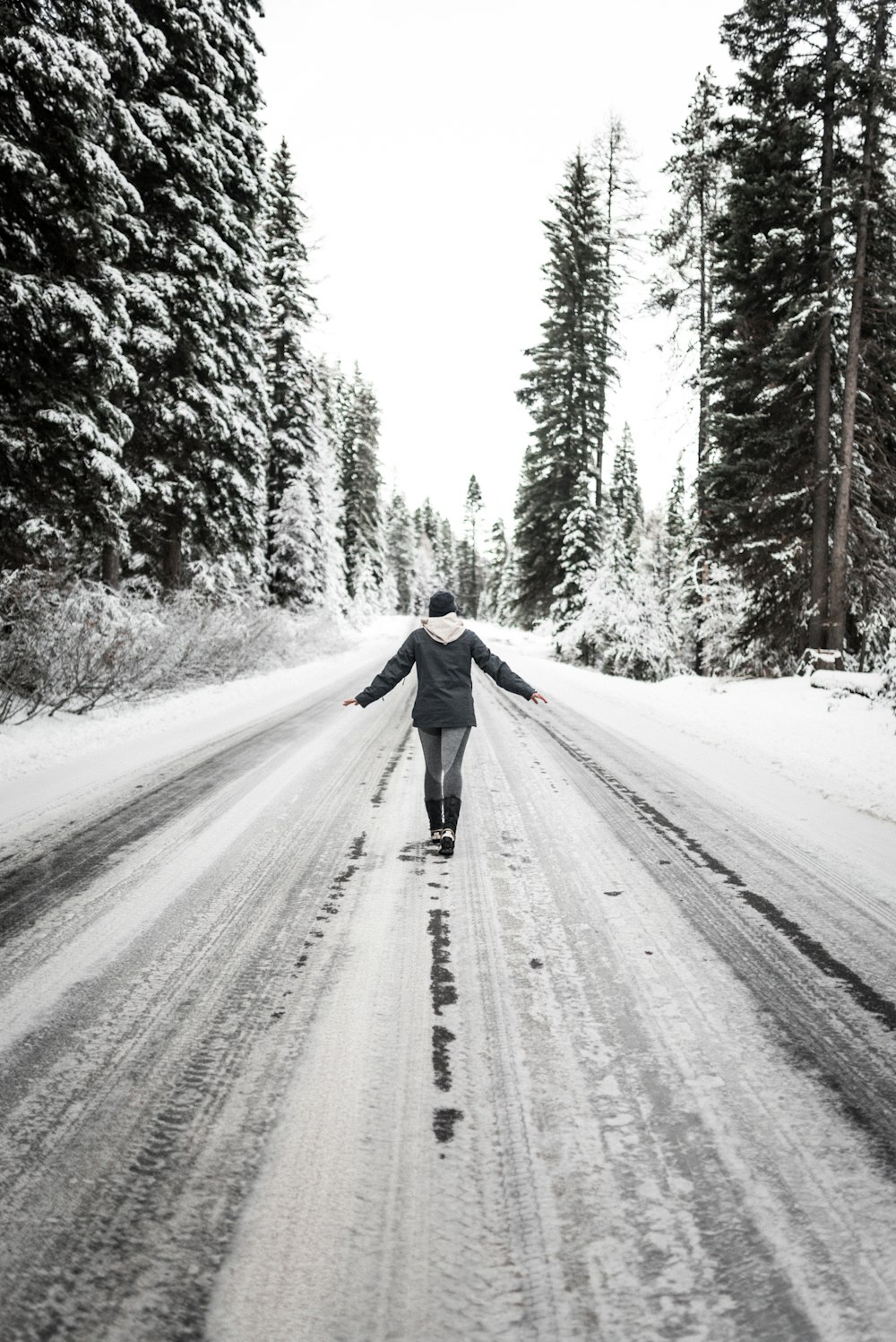 person in black jacket walking on snow covered road during daytime