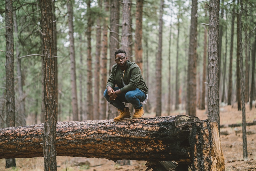 man in black jacket sitting on brown log during daytime