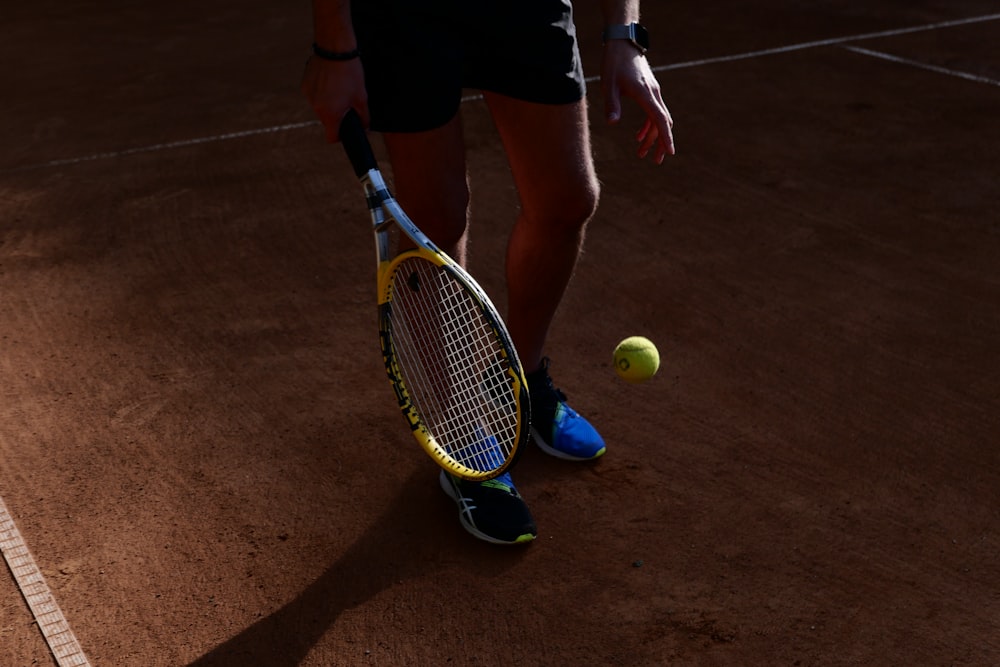 pessoa em shorts pretos segurando raquete de tênis amarela
