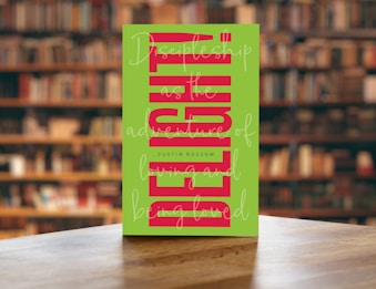 A book with a green cover featuring bold, vertical red text and cursive white writing overlaying the main title. The book is placed on a wooden table with a blurred background of bookshelves filled with books in a library setting.
