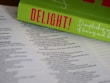 An open Bible lies on a surface, with the pages in focus. Resting on top is a bright green book titled 'DELIGHT!' in bold pink letters. The book cover includes cursive white text that reads 'Discipleship as a Way of Loving and...' The composition highlights religious and inspirational themes.