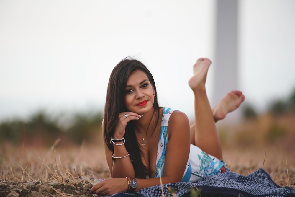 donna in abito senza maniche floreale blu e bianco che si siede sull'erba marrone durante il giorno