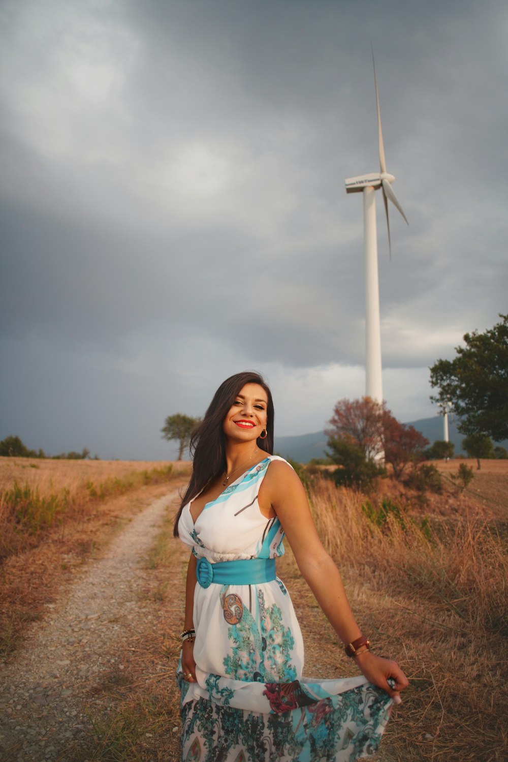 woman in white and blue floral sleeveless dress standing near white wind mill under gray cloudy