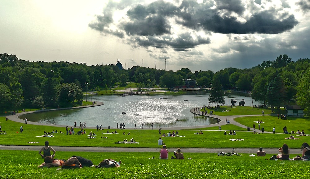pessoas no campo de grama verde perto do lago sob o céu nublado durante o dia