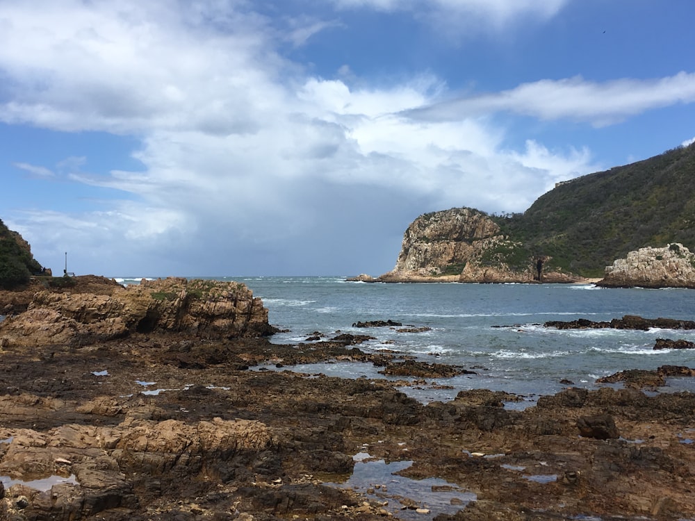 Formación rocosa marrón en el mar bajo el cielo azul y nubes blancas durante el día