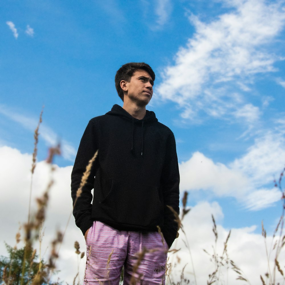 man in black hoodie standing on grass field under blue sky during daytime