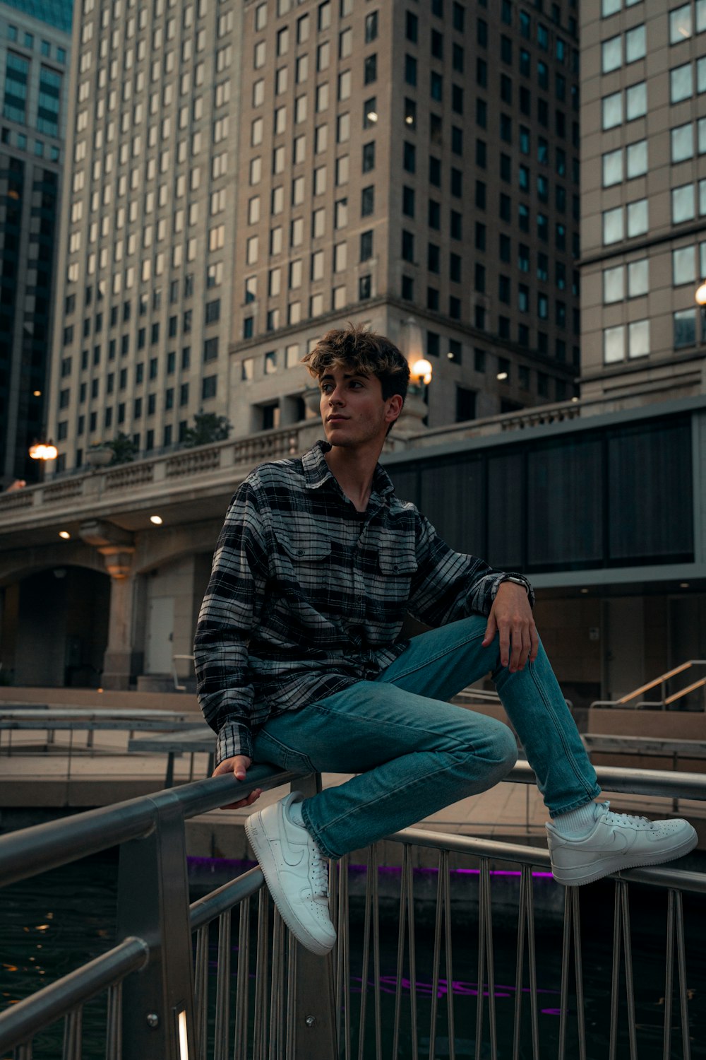 man in black and white plaid dress shirt and blue denim jeans sitting on gray metal