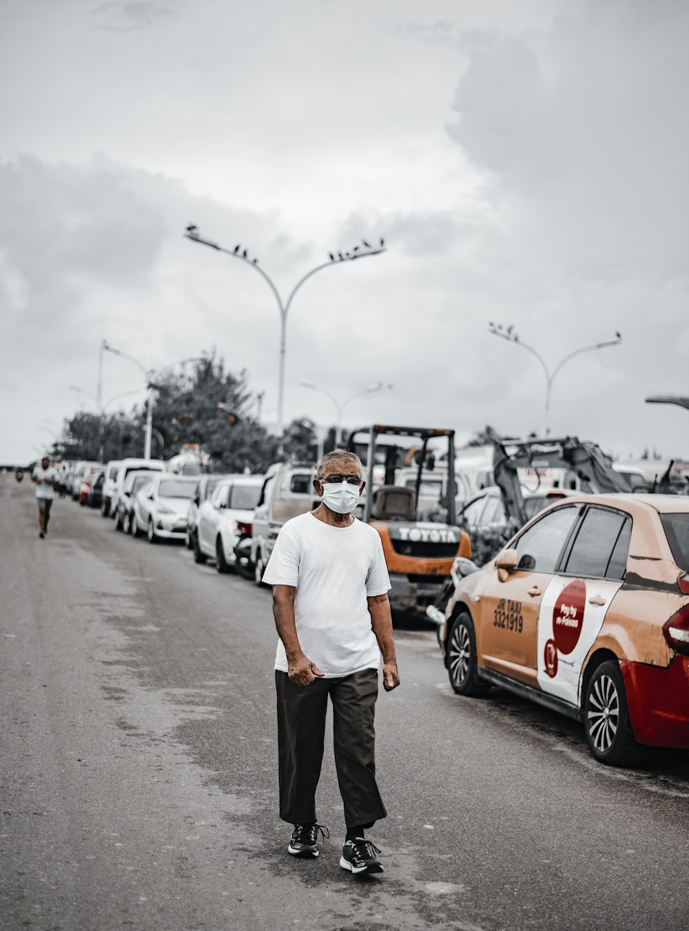 Hombre con camiseta blanca de cuello redondo y pantalones negros de pie junto a un coche naranja y blanco