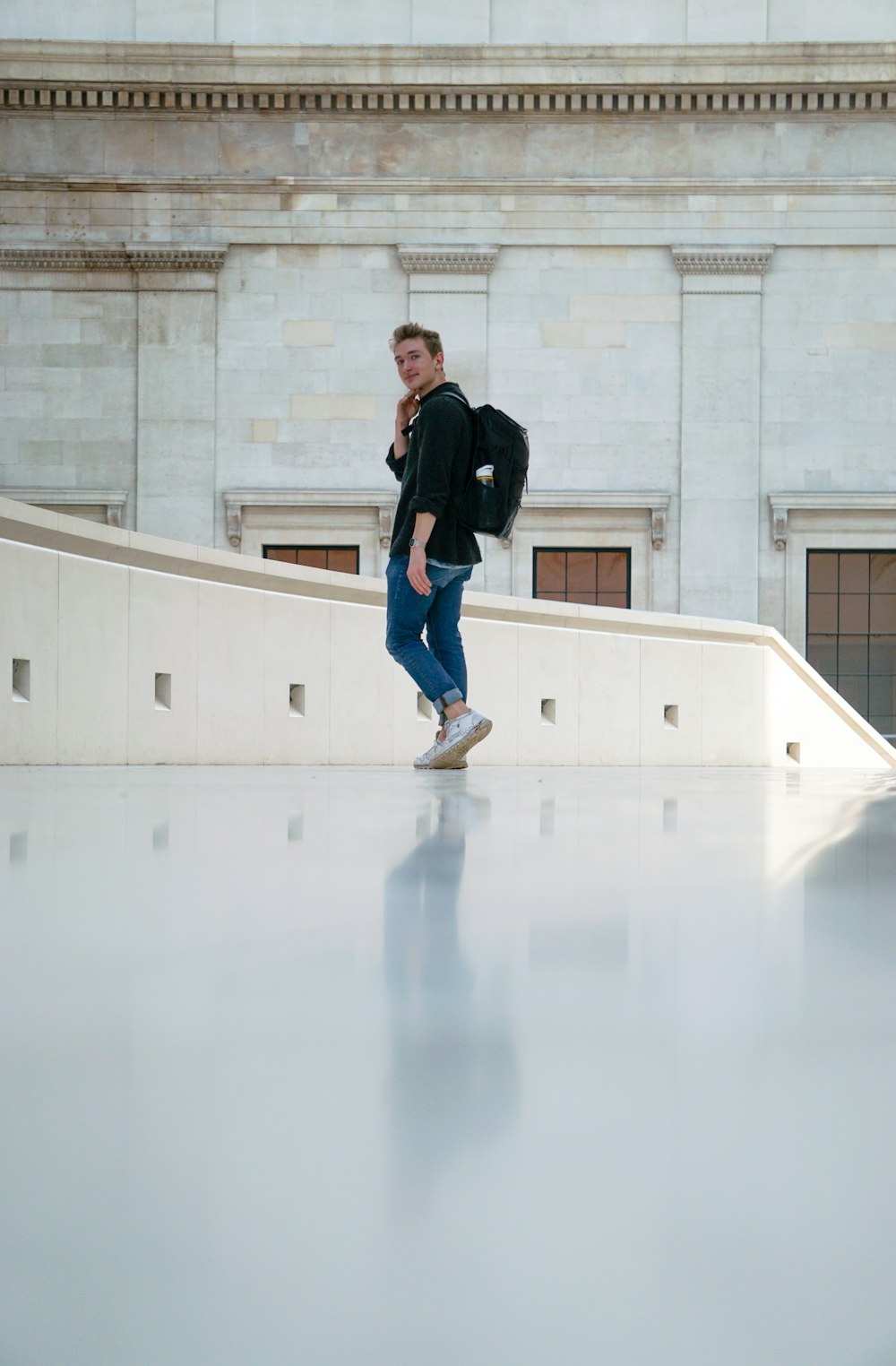 uomo in giacca nera e jeans blu denim che cammina sul pavimento bianco