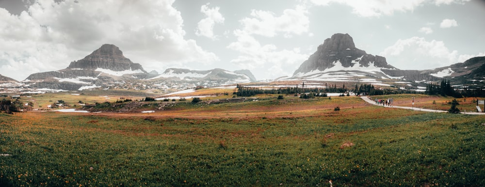 green grass field near mountain under white clouds during daytime