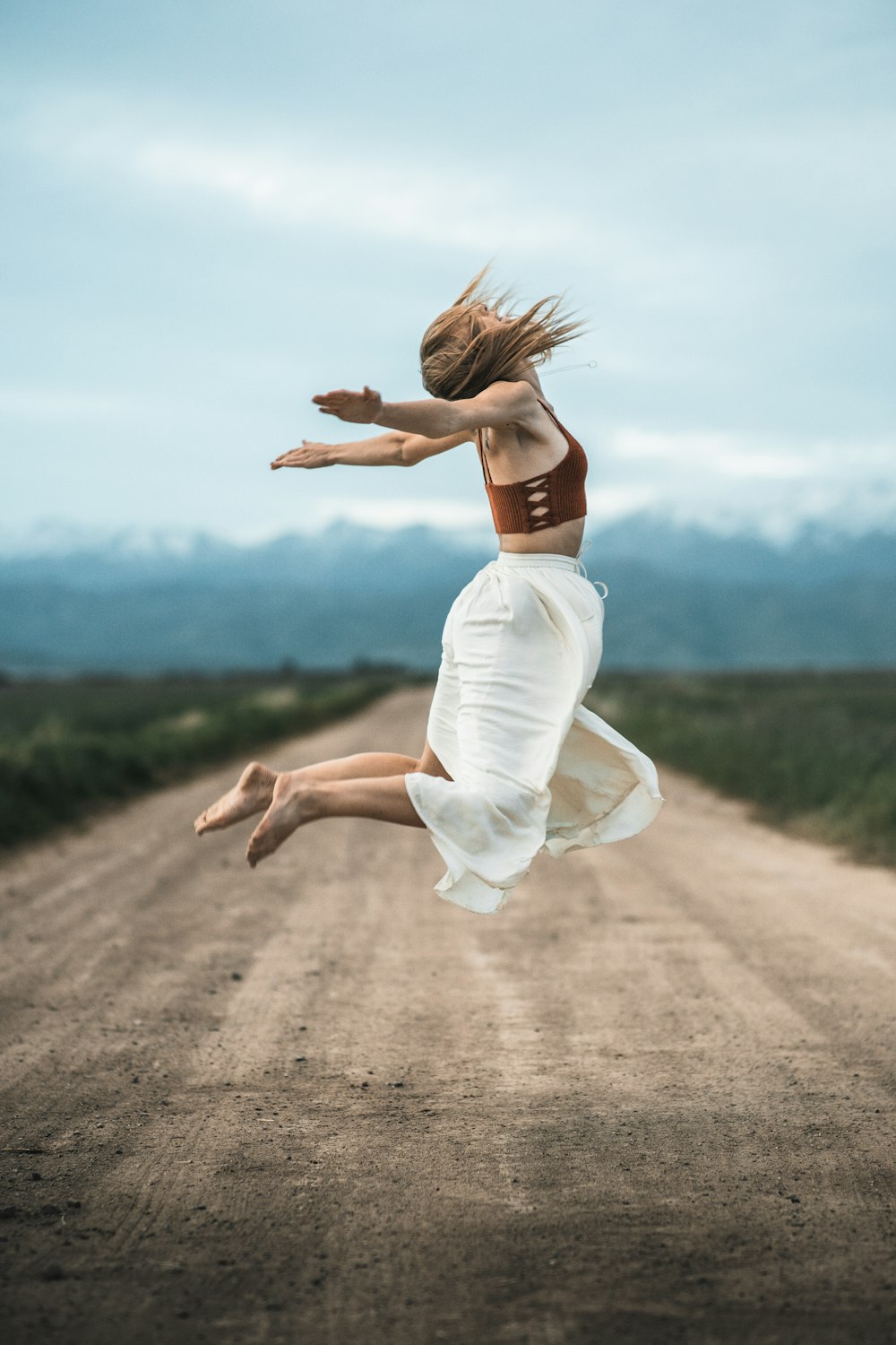 Frau in weißem Kleid läuft tagsüber auf braunem Feldweg