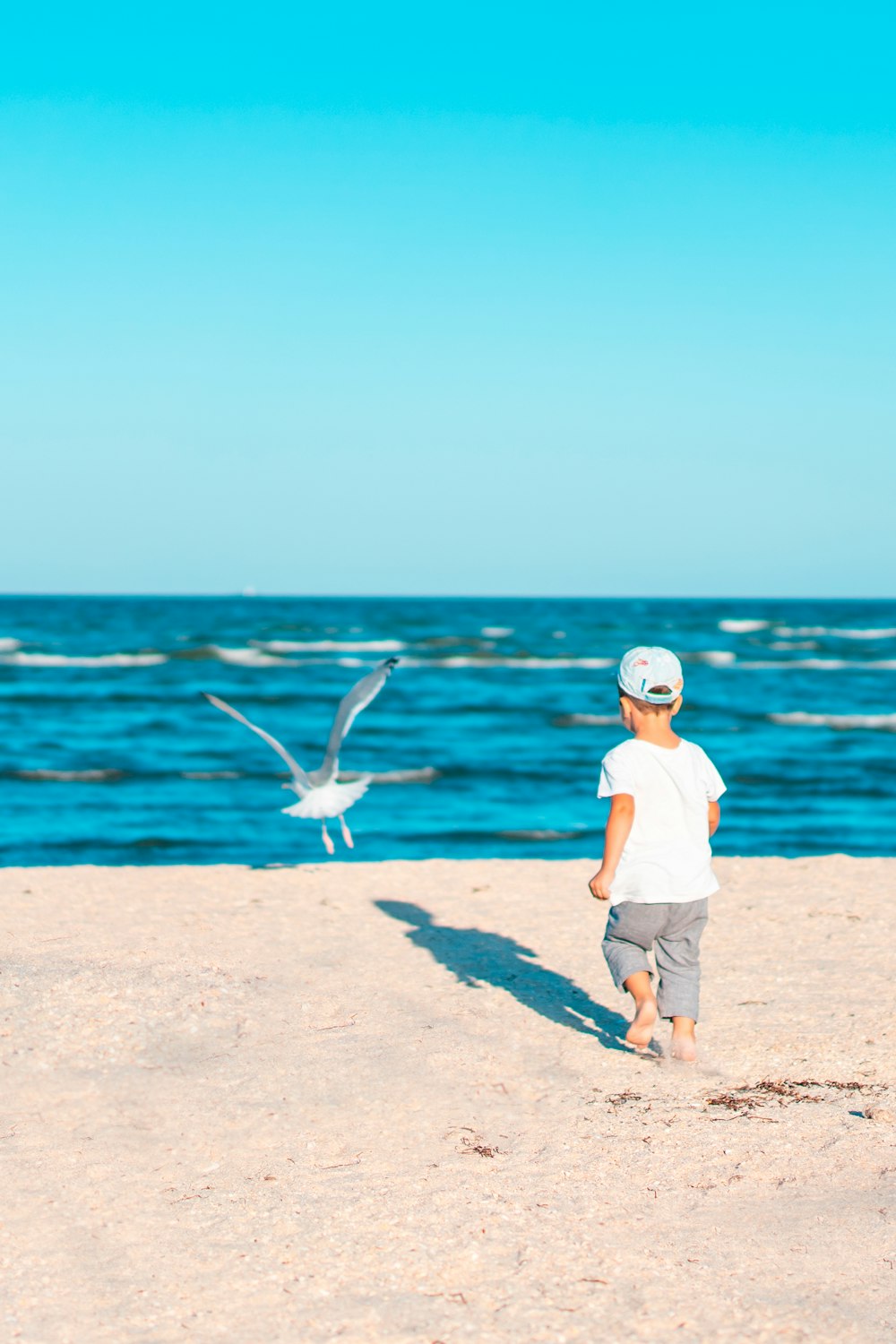 Junge in weißem T-Shirt und braunen Shorts auf braunem Sand in der Nähe von Wasser