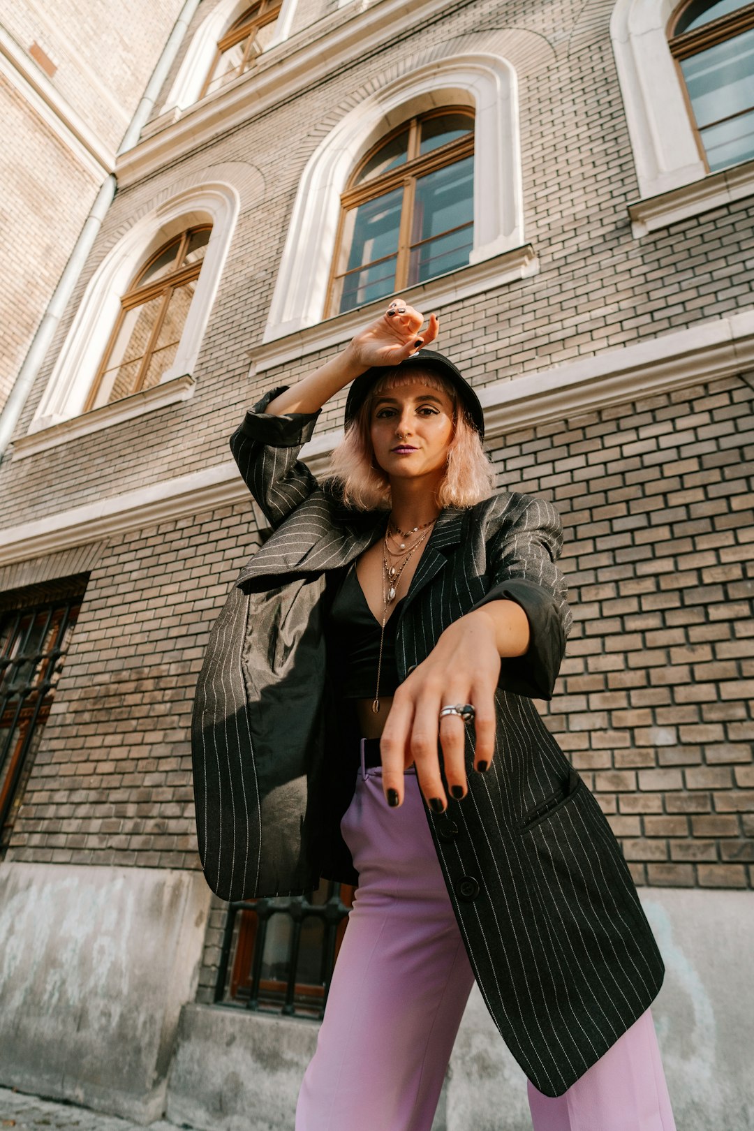 woman in gray coat standing beside brown brick building during daytime