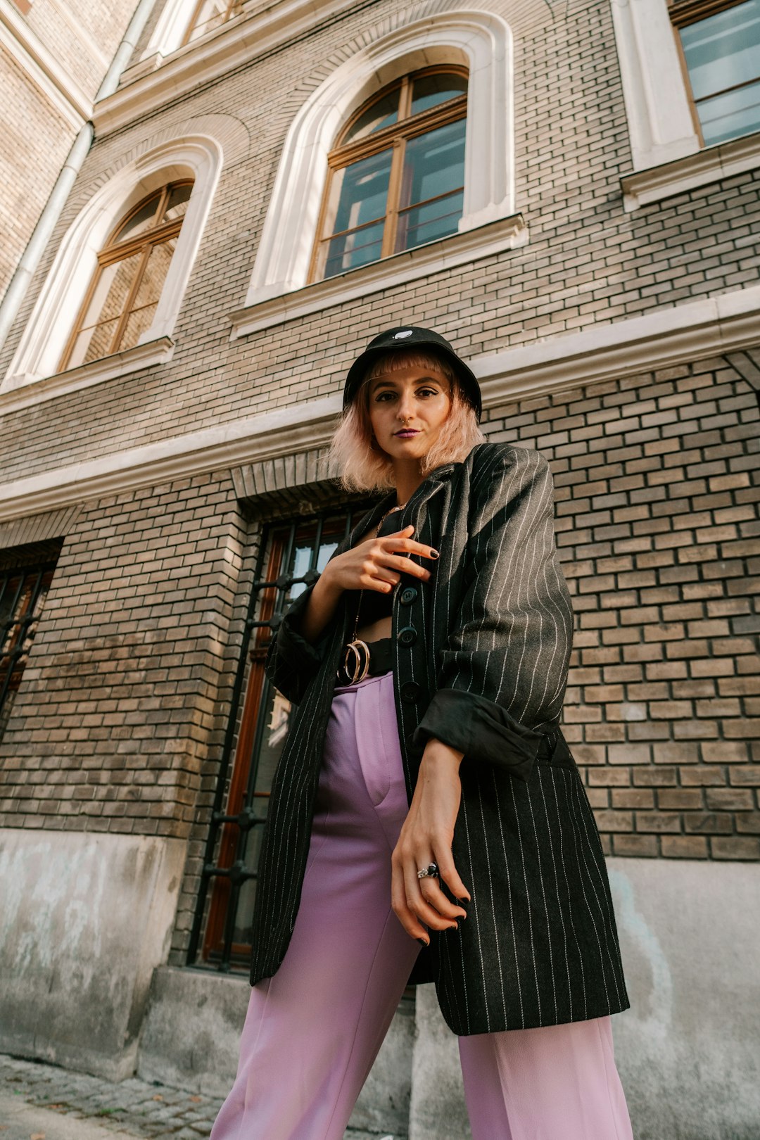 woman in black leather jacket standing beside brown brick building during daytime