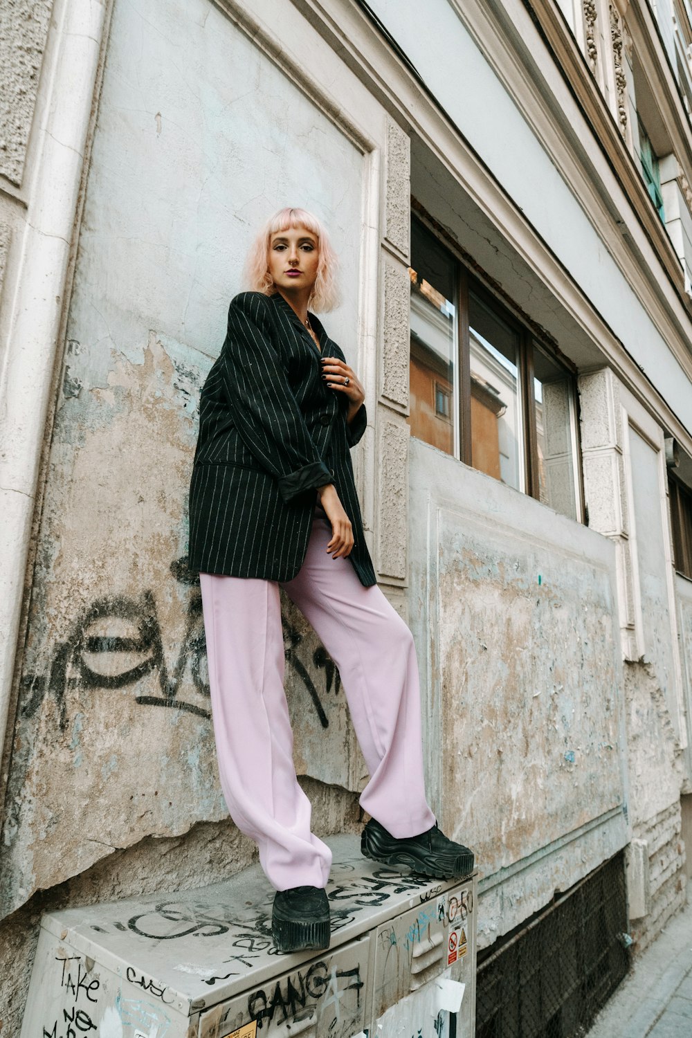 woman in black jacket and pink pants standing beside white concrete building during daytime