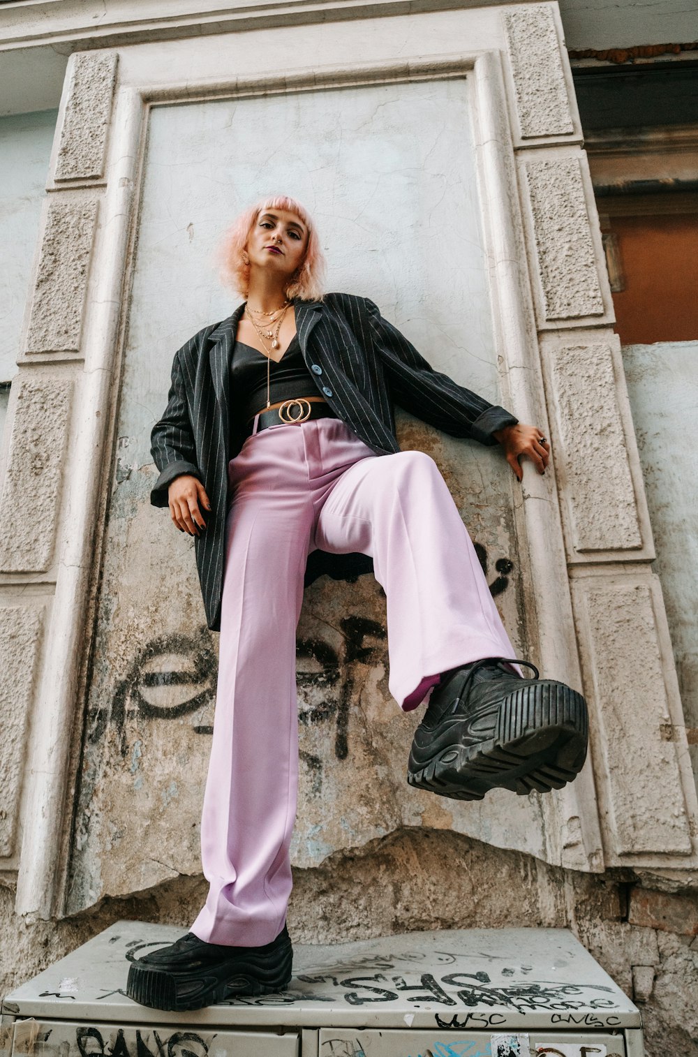 woman in black leather jacket and pink pants sitting on concrete wall during daytime