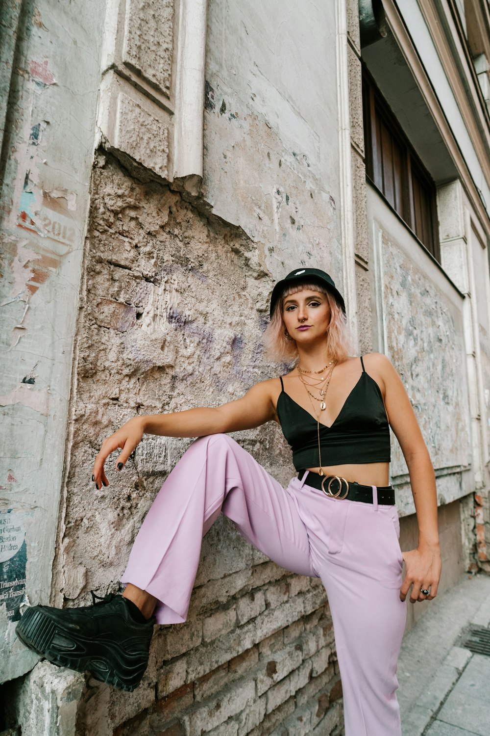 woman in black spaghetti strap top and pink pants sitting on concrete wall during daytime