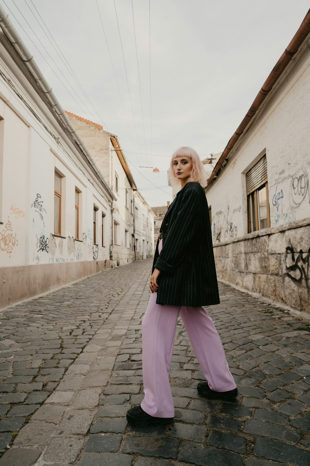 woman in black long sleeve shirt and pink pants standing on gray brick pavement during daytime