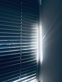 Vertical blinds partially closed with light streaming through, casting shadows and creating a serene atmosphere.