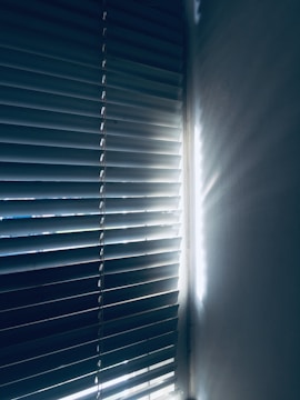 Vertical blinds partially closed with light streaming through, casting shadows and creating a serene atmosphere.