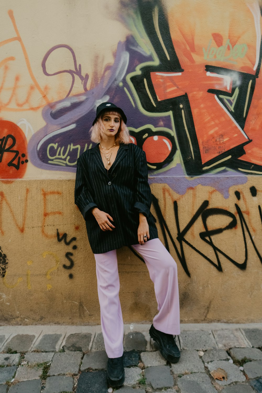 woman in black jacket and white pants standing beside wall with graffiti