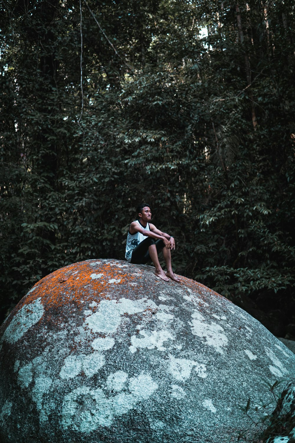 woman in black tank top and blue denim jeans sitting on rock