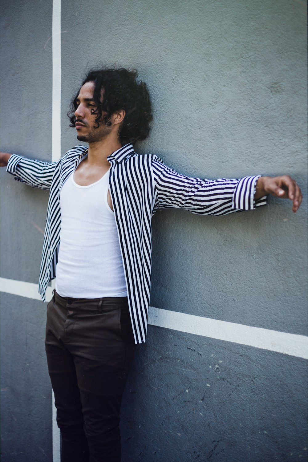 woman in white and black striped long sleeve shirt and black pants standing beside gray wall