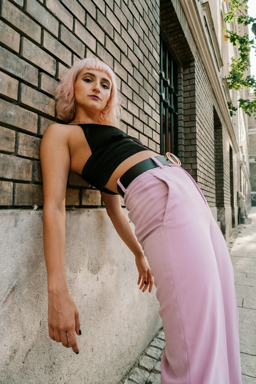woman in black brassiere and pink skirt leaning on gray concrete wall during daytime
