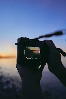 Close-up of hands holding a camera, capturing a sunset moment.