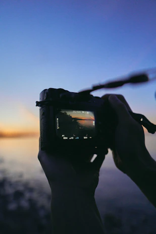 Close-up of hands holding a camera, capturing a sunset moment.