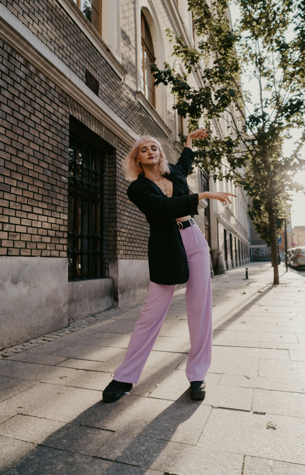 Femme en chemise noire à manches longues et pantalon rose debout sur le trottoir pendant la journée